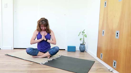 yoga teacher sitting on yoga mat with head bowed 
